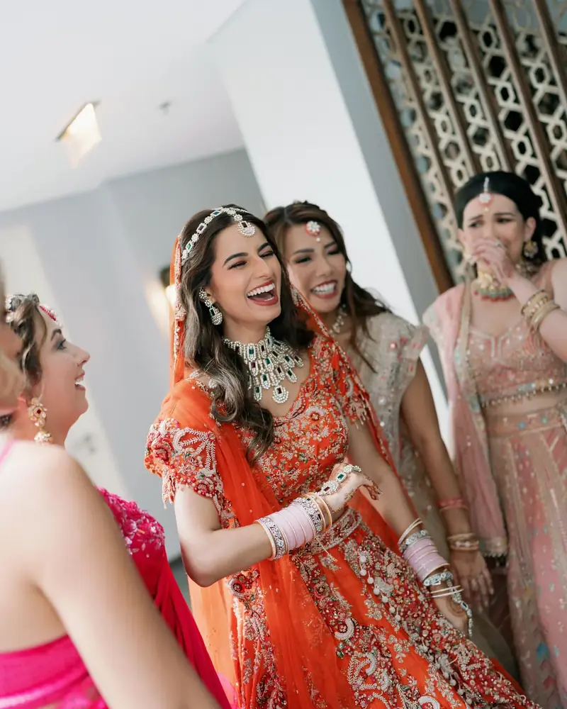A bride in a red lehenga laughing with her bridesmaids