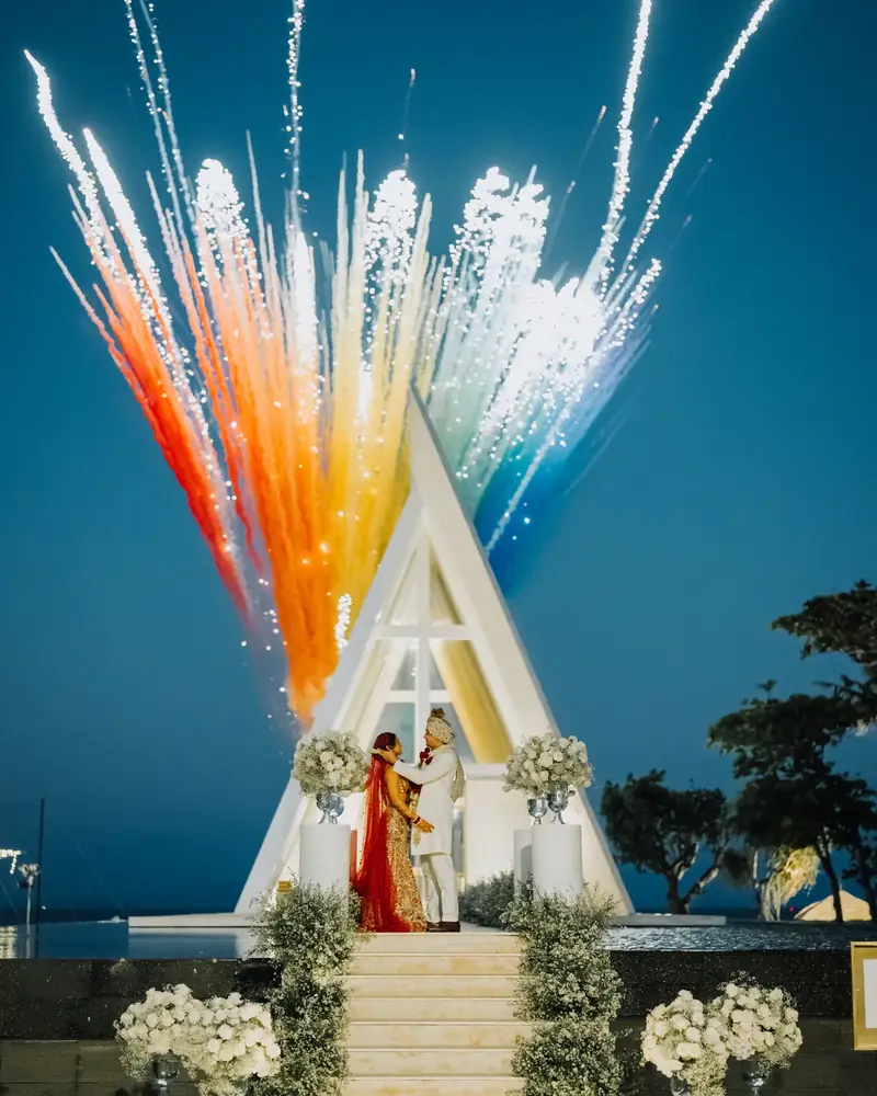 Fireworks over a glass chapel at dusk as the couple stand at the altar