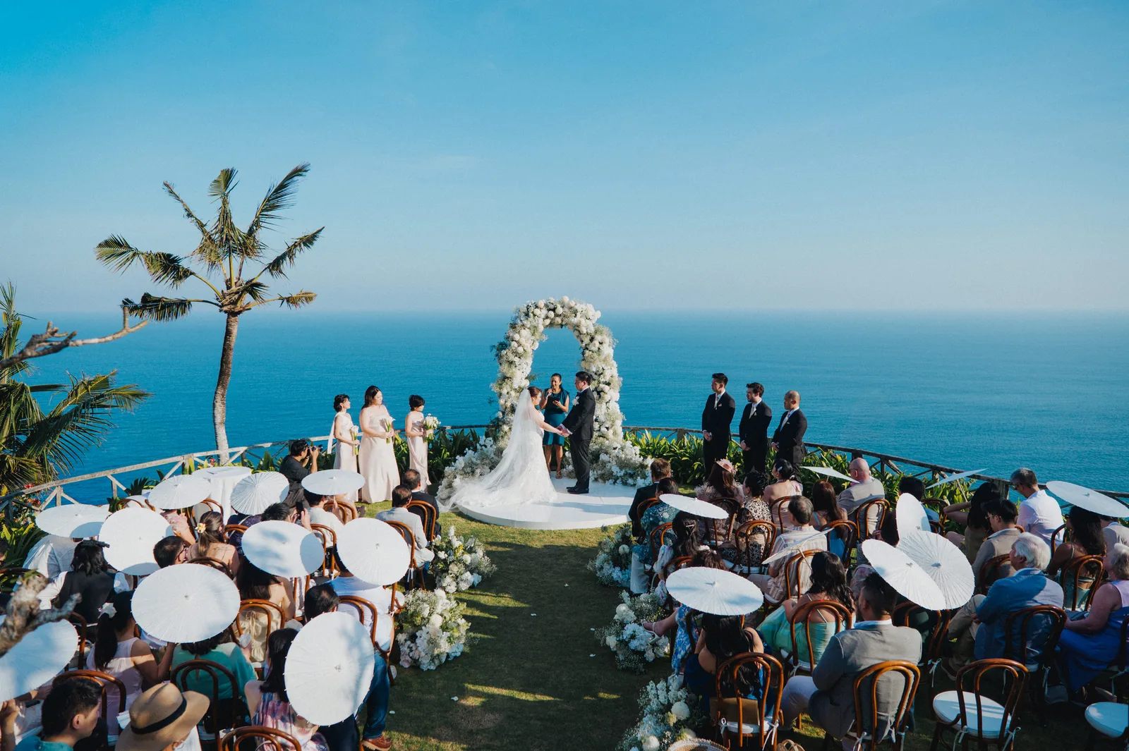 A clifftop ceremony at Khayangan Estate, guests seated around the floral arch above deep blue ocean